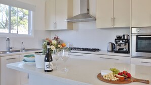 A modern kitchen with a large island, stainless steel appliances, and a view of the outdoors. - Cheerful Cottage Perfect for groups - Pool Table, Fire pit, Wifi & AC (Cessnock)