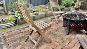 A patio with two wooden chairs, a fire pit, and a garden with raised beds and plants. - Cheerful Cottage Perfect for groups - Pool Table, Fire pit, Wifi & AC (Cessnock)