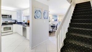 A modern kitchen with white cabinets, a microwave, and a dishwasher. There is a dining area with a table and chairs, and a staircase with black carpeted steps. - Endless Summer,Jupiter Walk to Beach & Restaurants! (Jupiter)