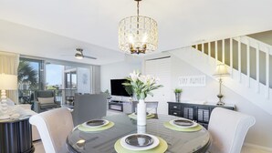 A modern dining area with a round glass table, white upholstered chairs, a decorative vase, and a chandelier. - Endless Summer,Jupiter Walk to Beach & Restaurants! (Jupiter)