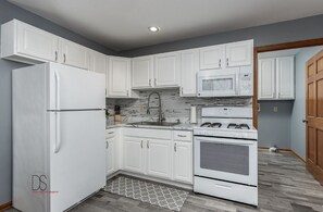 Una cucina moderna con mobili bianchi, un lavello in acciaio inossidabile, un forno a microonde e un piano cottura a gas.