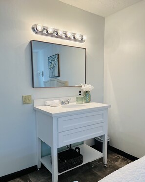 A bathroom with a white vanity, a large mirror, and a lighted vanity mirror. - EC Reed's Mercantile and Hotel (Marble Hill)