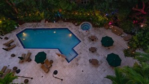 A rectangular pool with a small circular hot tub, surrounded by lounge chairs and umbrellas, set in a lush garden with dense foliage. - Your Bay View Escape in Coconut Grove, Pool & Gym (Miami)