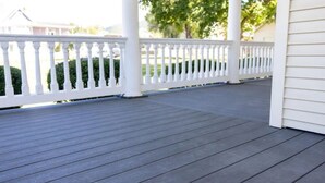 A covered porch with a wooden deck and white railings.