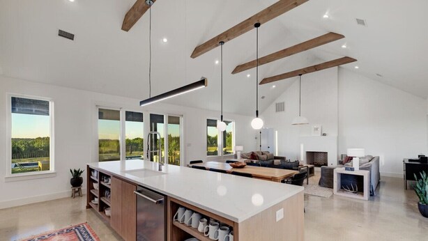 Una cocina amplia con una isla grande, vigas de madera y ventanas grandes que ofrecen vistas al exterior.
