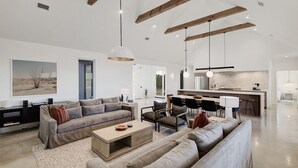 Un salón amplio con un sofá grande, una mesa de centro y una zona de comedor con sillas, y una cocina al fondo.