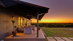 Una casa moderna con un porche cubierto, mobiliario exterior y vistas al atardecer.