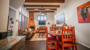 Un salón amplio con techo alto, una zona de comedor con sillas de madera y mantel colorido, y un cuadro grande de un toro en la pared.