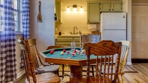 A pool table with billiard balls, wooden chairs, a kitchen with a sink and cabinets, and a window with checkered curtains. - The Woodland Cottage Smoky Mountain Hideaway (Sevierville)