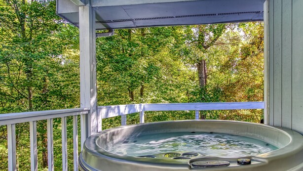 A hot tub on a wooden deck with a white railing, surrounded by trees. - The Woodland Cottage Smoky Mountain Hideaway (Sevierville)