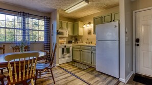 A kitchen with wooden flooring, a dining table with chairs, a refrigerator, and green cabinets. - The Woodland Cottage Smoky Mountain Hideaway (Sevierville)