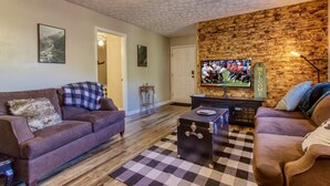 A living room with two sofas, a television, a wooden accent wall, and a checkered rug. - The Woodland Cottage Smoky Mountain Hideaway (Sevierville)