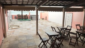 A covered outdoor seating area with stone flooring and wooden furniture.