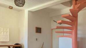 A modern interior with a wooden bench, a small sailboat model, wicker ottomans, and a unique pink spiral staircase.