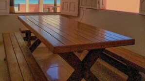A room with a wooden table and benches, large windows with views of the beach and ocean, and a thatched roof structure.