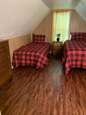 Una habitación pequeña y acogedora con dos camas, paredes de madera, una ventana con cortinas, una mesita de noche y un aparador.