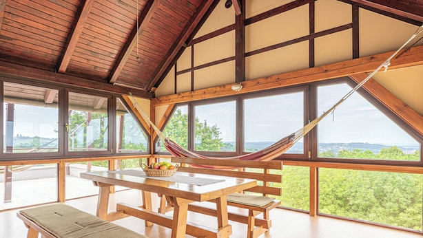 Un intérieur en bois, de grandes fenêtres, un hamac et une table avec un panier de fruits.