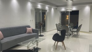 A modern living room with a grey sofa, a glass coffee table, and black chairs. There is a dining area with a glass table and chairs. - 5 minutes from la caleta beach 10 minutes from casa de campo la romana (romana del este)