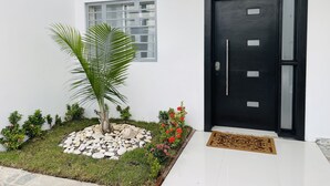 A modern entrance with a black door, a small window, a palm tree, and a welcome mat. - 5 minutes from la caleta beach 10 minutes from casa de campo la romana (romana del este)