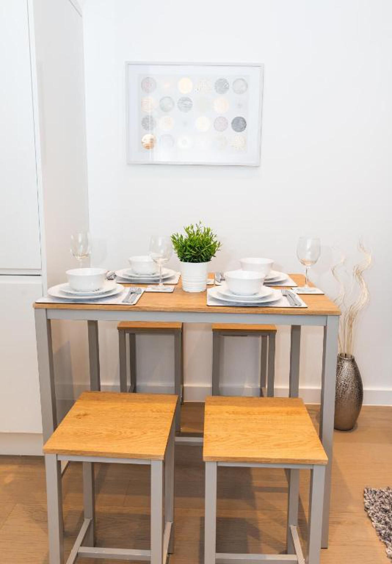 Comedor con una mesa lista para cuatro personas, incluyendo platos, vasos y una pequeña planta en maceta.