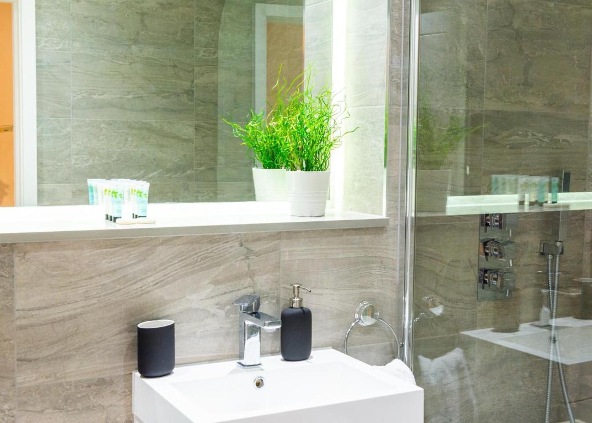 Une salle de bain moderne avec un lavabo blanc, un robinet chromé et une plante en pot posée sur le rebord de la fenêtre.