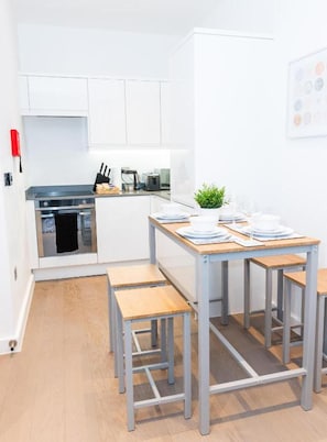 Une cuisine moderne avec des meubles blancs, une cuisinière en acier inoxydable et un petit coin repas comprenant une table et des bancs.