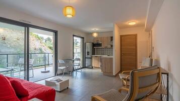 Een modern appartement met balkon, keuken en woonruimte met een rode bank en houten stoelen.