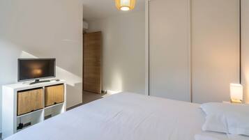 Ein modernes Hotelzimmer mit einem großen Bett, einem Flachbildfernseher auf einer weißen Kommode, einer Nachttischlampe und einem Kleiderschrank.