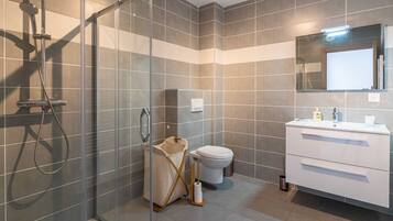Een moderne badkamer met een douchecabine van glas, een wit toilet en een witte wastafel met spiegel.
