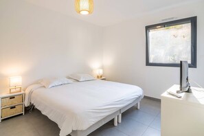 Ein Schlafzimmer mit einem Bett, zwei Nachttischlampen, einem Schreibtisch mit Computer und einem Fenster mit Blick.