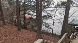 A wooden deck leading to a lake with trees and a building with a red roof in the background. - Toledo Bend on Lanana Bay Waterfront Camp Boathouse Dock Subdivision Boat Launch (Many)