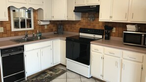 Una cocina con armarios blancos, una estufa negra, un microondas y un lavamanos.