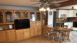 Una cocina con gabinetes de madera, una mesa de comedor con sillas, un ventilador de techo y un televisor.
