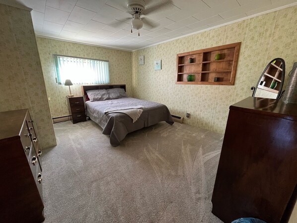 Une chambre à coucher comprenant un lit, une commode, une table de chevet et une étagère fixée au mur.