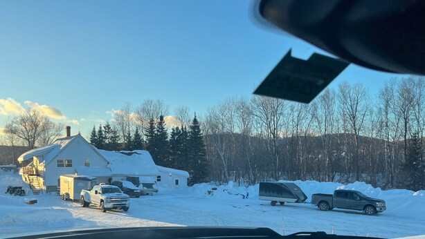 Zona residencial cubierta de nieve, con casas, vehículos estacionados y cielo despejado.