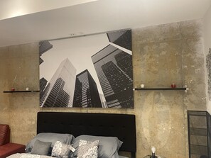 A bedroom with a large bed, a headboard, and a cityscape painting on the wall.