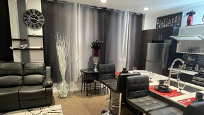 A modern living room with a sofa, dining table, and chairs. There is a clock on the wall and a vase with branches. - Mr. Whips Family Fun House 3,000 Sq Ft Game unit with arcade room and rear yard (Philadelphia)