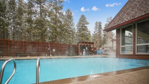 A swimming pool with a wooden deck, a covered seating area, and a building with large windows. - Quick Walk to lift and town (Breckenridge)