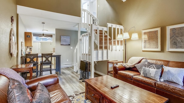 A cozy living room with a brown leather sofa, a wooden coffee table, and a dining area with a table and chairs. - Quick Walk to lift and town (Breckenridge)