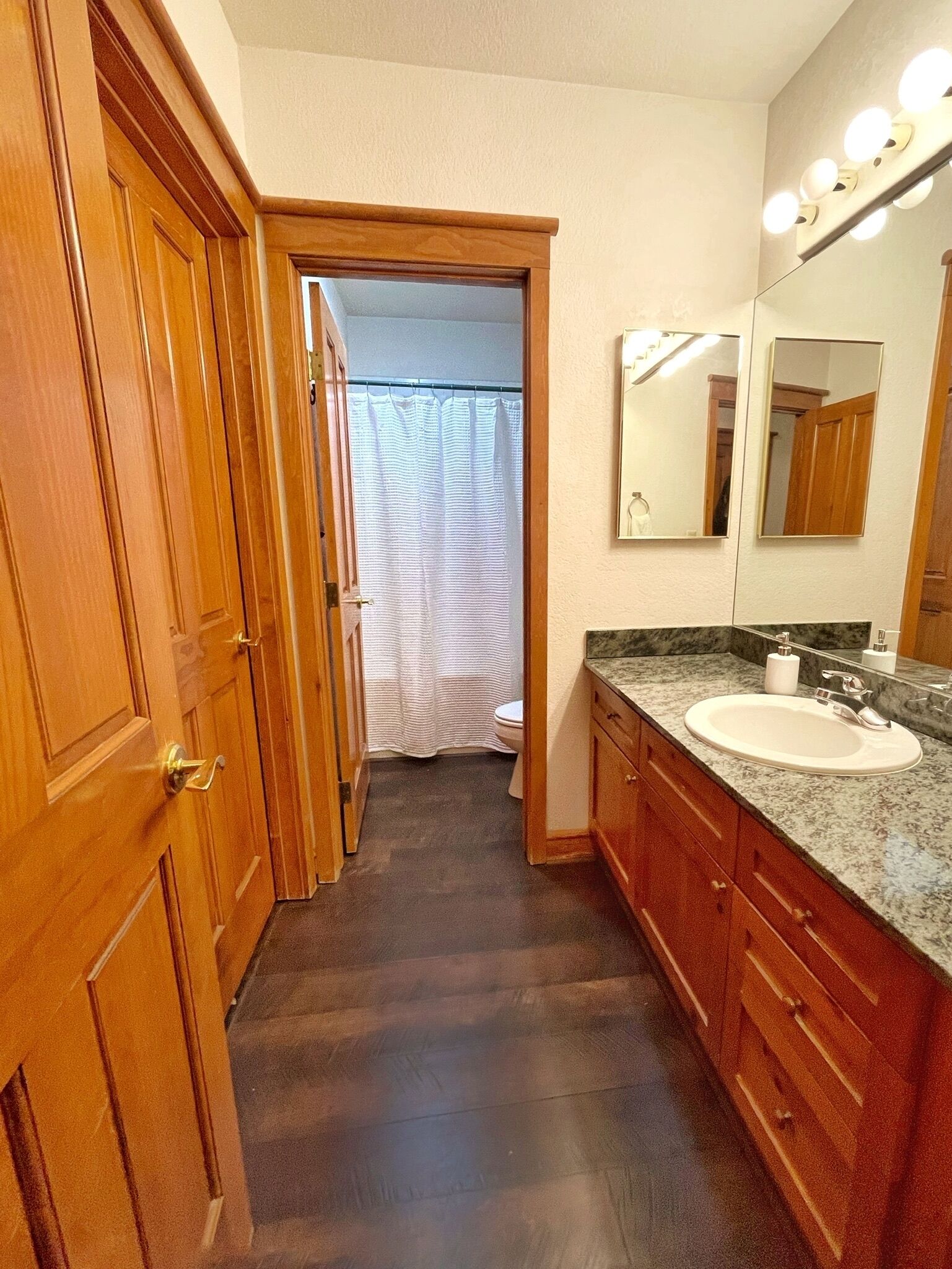 A bathroom with wooden cabinets, a marble countertop, a sink, and a mirror with lights.