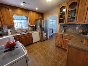 A kitchen with wooden cabinets, a stainless steel refrigerator, a dishwasher, and a red kettle on the stove.