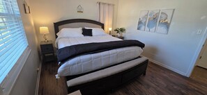 A neatly made bed with a headboard, a bedside lamp, and a small table with a plant.