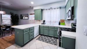 A modern kitchen with green cabinets, a white countertop, and a black and white patterned rug. - Friends, Family & Dog Stay in Monterey Peninsula with AC & Grill (Salinas)