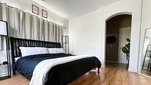 A neatly made bed with a black headboard and white bedding, a wooden floor, and a white wall with a framed picture and a mirror. - Friends, Family & Dog Stay in Monterey Peninsula with AC & Grill (Salinas)