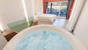 Ein modernes Schlafzimmer mit einer großen Badewanne, einem Balkon mit Tisch und Stühlen sowie einem Bett mit weißen Leinen.