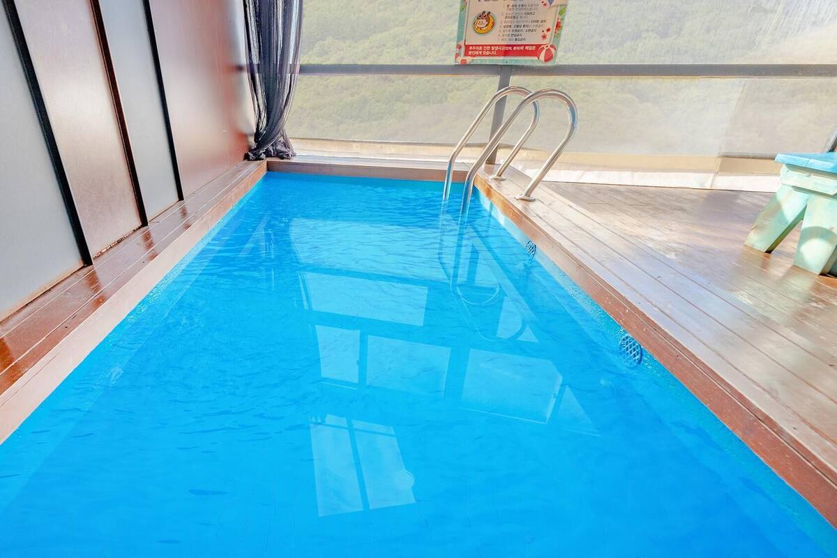 Ein klares, blaues Hallenbecken mit Metallleitern an einer Seite und einem Holzterrasse auf der anderen Seite.