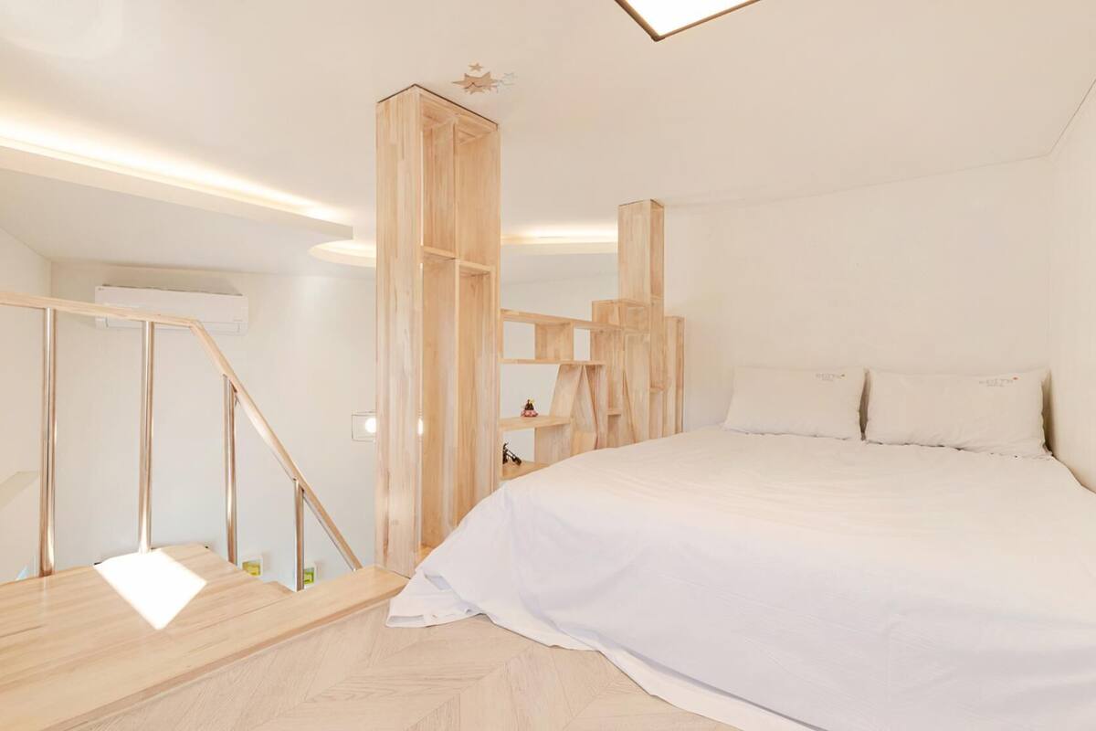 Ein modernes Schlafzimmer mit einer Holztreppe, einem Bett mit weißer Bettwäsche und einem minimalistischen Design.