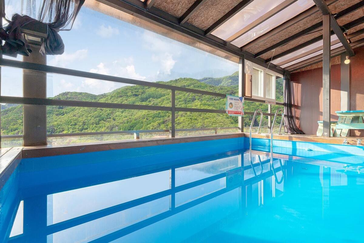 Ein Swimmingpool mit Blick auf grüne Hügel, einer Holzterrasse und einem Picknicktisch.