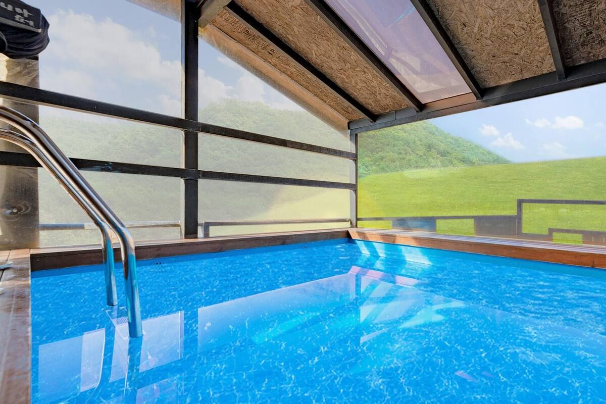 Ein Innenpool mit klaren Glaswänden, einer Holzterrasse und Blick auf eine grüne Landschaft.