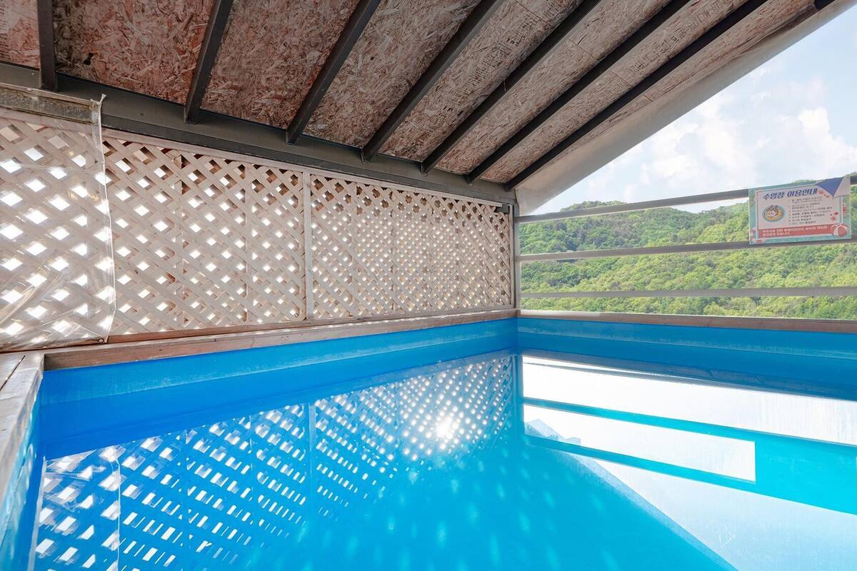 Ein Pool mit klarem, blauem Wasser, umgeben von einer Holzterrasse und einem Gitterzaun.